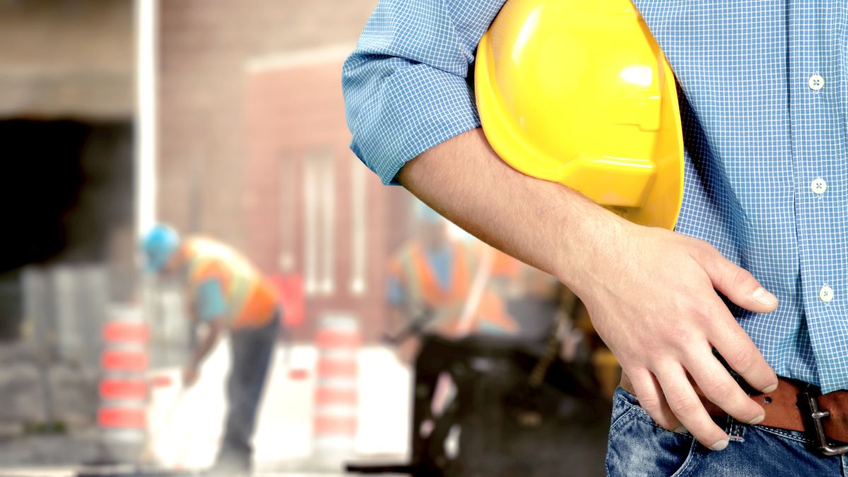 Trabalhador segurando capacete de segurança em ambiente industrial, representando prevenção de riscos ocupacionais e normas trabalhistas. trabalho